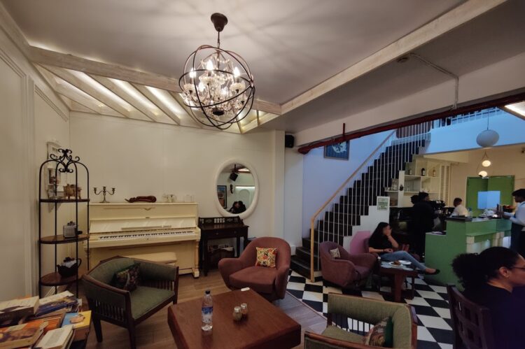 Vintage themed cafe lounge with upright piano, spherical chandelier, wrought-iron shelving and checkered flooring designed by Nail and Hammer